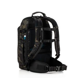 Tenba Axis v2 20L Backpack MultiCammusta -kamerareppu on varustettu mustalla ja tummalla camokuviolla, pehmustetuilla olkahihnoilla, selkäpehmusteilla, lantiovyöllä ja useilla lokeroilla, kuvassa pystyssä valkoista taustaa vasten.