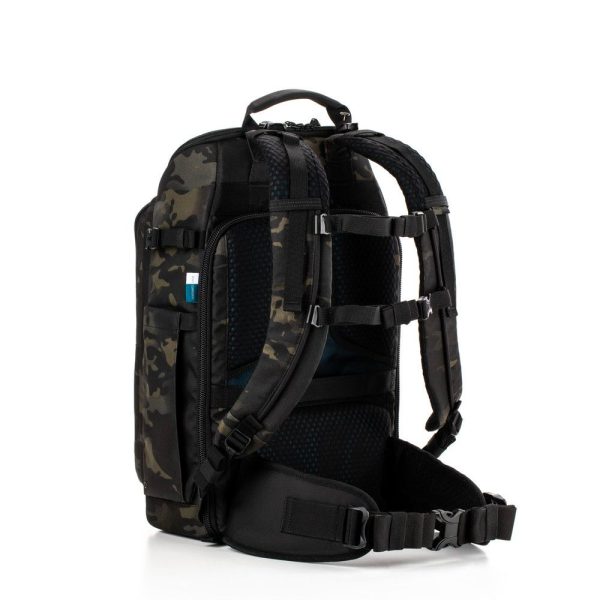 Tenba Axis v2 20L Backpack MultiCammusta -kamerareppu on varustettu mustalla ja tummalla camokuviolla, pehmustetuilla olkahihnoilla, selkäpehmusteilla, lantiovyöllä ja useilla lokeroilla, kuvassa pystyssä valkoista taustaa vasten.