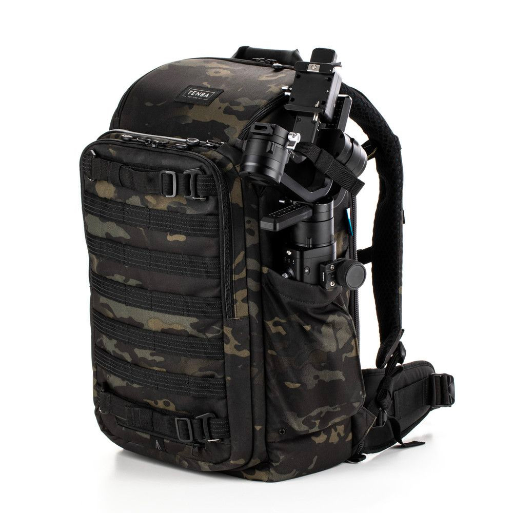 Tenba Axis v2 24L reppu MultiCammusta -kamerareppu, jossa on musta naamiointi, useita vetoketjulokeroita ja MOLLE-verkko, pitää sisällään sivulleen kiinnitetyn kameragimbalin.