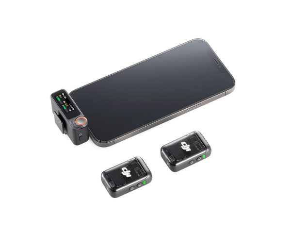 Älypuhelin kytketty DJI Mic 2 Dual Kit -langaton mikrofonijärjestelmä vastaanotin, jossa on kaksi kompakti musta langaton lähetin sijoitettu lähelle valkoiselle pinnalle.
