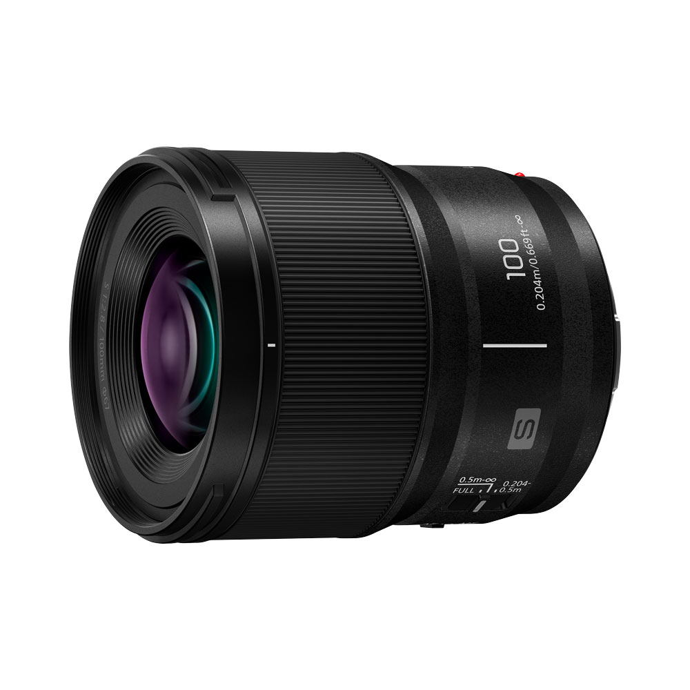 The Panasonic Lumix S 100mm F/2.8 macro lens is a black lens with "100" and "0.20m/0.66ft" printed on the side, a textured focus ring and a reflective glass element against a white background.