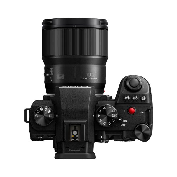 Top view of a black Panasonic digital camera with a Panasonic Lumix S 100mm F/2.8 macro lens attached, showing the controls, buttons and on/off switch on the right.