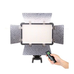 Godox LED 308C II suorakulmainen studiovalo, jossa on neljä säädettävää hopeista lato-ovea ja kädessä pidetty digitaalinen kaukosäädin valkoista taustaa vasten.