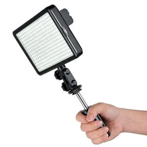 Kädessä on Godox Led 308C, suorakulmainen LED-videovalaisinpaneeli, jossa on monia pieniä LED-valoja, jotka on järjestetty ruudukkoon, ja joka on kiinnitetty kahvaan, jossa on säädettävä kiinnike.