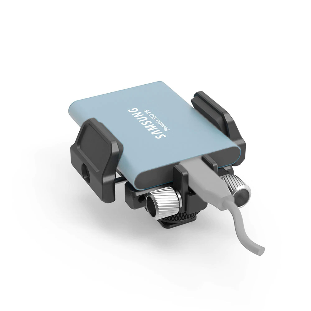 Vaaleansininen Samsungin kannettava SSD-levy on kiinnitetty ulkoisen SSD-levyn SmallRig 2343 Universal Holder for External SSD -pidikkeeseen, ja siihen on kiinnitetty harmaa kaapeli, eristettynä valkoiselle taustalle.