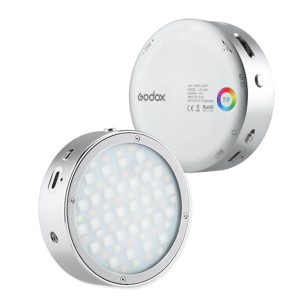Godox R1 + AK R1 -sarjassa on kaksi pyöreää, hopeista LED-videovalaisinta - toisessa näkyy etupuolen LED-verkko ja toisessa takapuoli, jossa on ohjauspainikkeet, väripyörä ja useita portteja.
