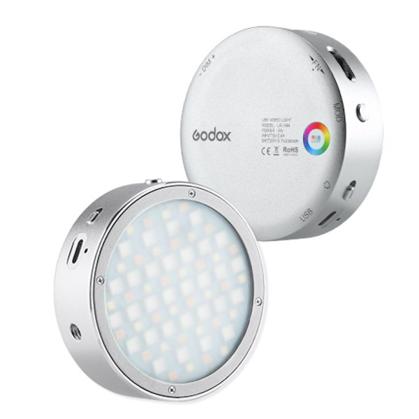 Godox R1 + AK R1 -sarjassa on kaksi pyöreää, hopeista LED-videovalaisinta - toisessa näkyy etupuolen LED-verkko ja toisessa takapuoli, jossa on ohjauspainikkeet, väripyörä ja useita portteja.