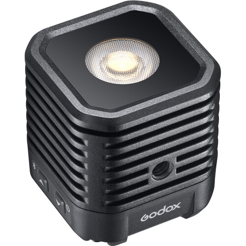 Godox WL4B Waterproof LED-valaisin on kompakti, musta, kuution muotoinen LED-valaisin, jossa on kuvioitu pinta, tuuletusaukot, sivusäätöpainikkeet ja pyöreä valopaneeli yläosassa.