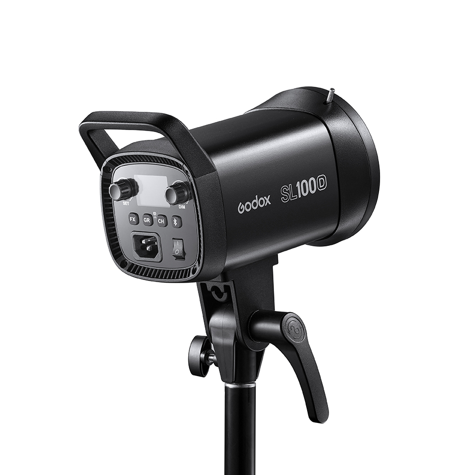 Musta Godox LED SL100D Daylight -LED-valo on asennettu jalustalle, ja se on kuvattu kulmassa, jossa näkyy sen ohjauspaneeli, säätönupit ja kahva.