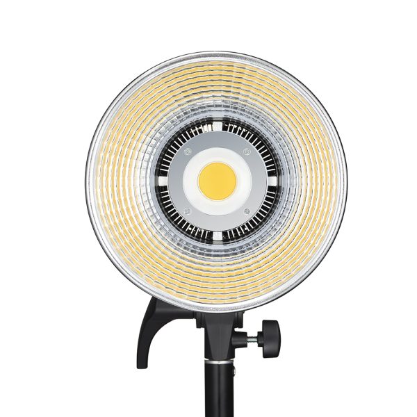 Godox LED SL100D Daylight on pyöreä LED-valaisin, jossa on keskittyvät keltaiset ja hopeiset renkaat ja joka on asennettu mustaan säädettävään jalustaan. Kuvassa edestä valkoista taustaa vasten.