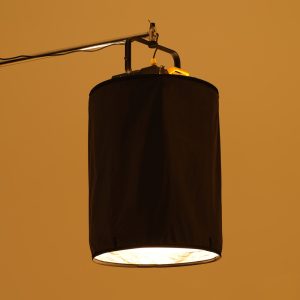 Godox P600BHSSS Black Opaque Skirt for P600Bi Hard peittää sylinterimäisen studiovalon, joka roikkuu metallisesta varresta ja heittää lämpimän alaspäin suuntautuvan valon kellanruskeaa taustaa vasten.