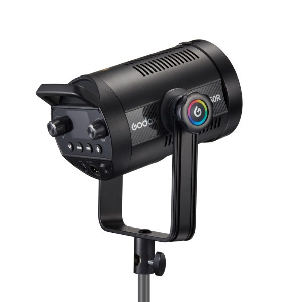 Mustan värinen Godox SL150R RGB LED -videovalaisin, jossa on säätönupit ja värikäs pyöreä painike, on asennettu jalustalle ja näytetään takaa valkoista taustaa vasten.