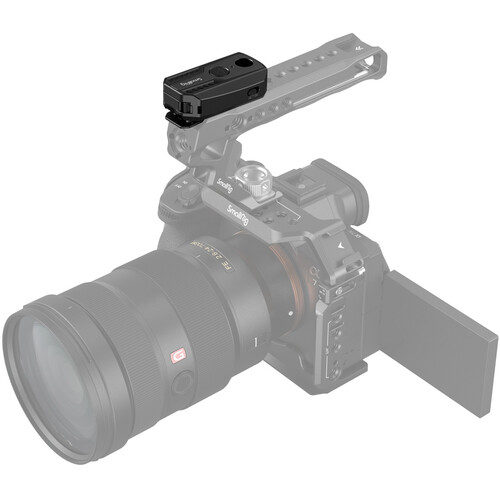 The compact black SmallRig 3902 wireless remote control is attached to the top handle of a digital camera with a large lens and flip-out display; the faded camera and handle accentuate the control.