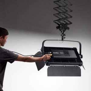 Henkilö liittää kaapelin Godox P200BI Studio LED-valopaneeliin, joka on kiinnitetty sisäänvedettävään kattokannattimeen neutraalia taustaa vasten.