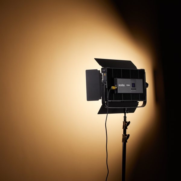 Godox P200BI Studio LED-valopaneeli ladonluukuilla on kytketty päälle, asennettu jalustalle ja säteilee kirkkaan, fokusoidun valonsäteen tavalliselle beigelle seinälle valokuvaus- tai videostudiossa.