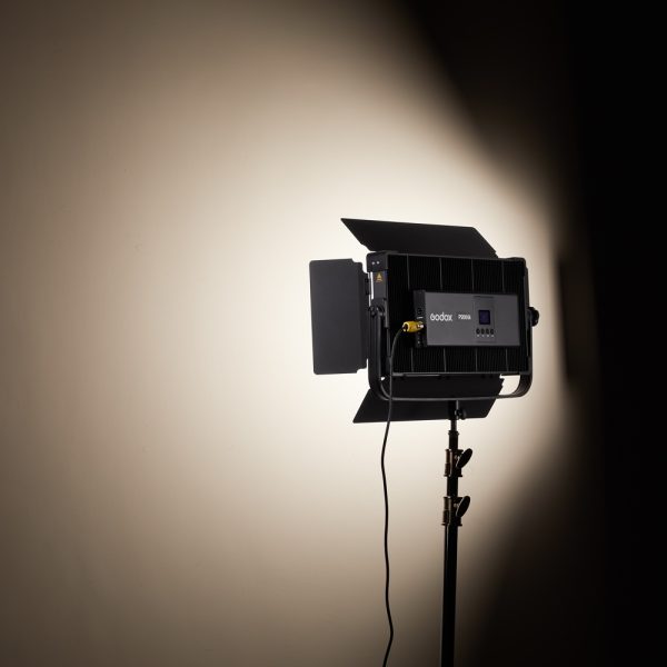Kolmijalkaiseen jalustaan asennettu Godox P200BI Studio LED-valopaneeli on kytketty päälle, ja se heijastaa kirkkaan, fokusoidun valonsäteen tavalliselle beigelle seinälle luoden pehmeän varjostuksen valaistun alueen ympärille.
