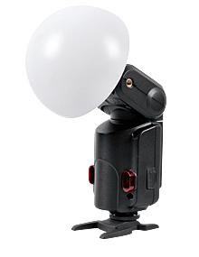 Godox Witstro Diffusor Ball, suuri valkoinen kupolimuotoinen kamerasalaman diffuusori, on kuvassa kiinnitettynä salamalaitteeseen ja asennettuna pieneen mustaan jalustaan valkoista taustaa vasten.