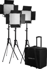 NANLITE 3 Light Kit 600CSA, jossa on kolme LED-paneelivaloa, joissa on ladon ovet säädettävissä jalustoissa, on esitetty mustan pyörillä varustetun NANLITE-merkityn ja olkahihnalla varustetun kärrylaukun vieressä.