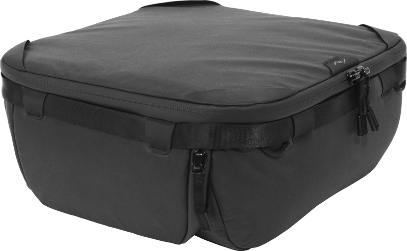 Peak Design Camera Cube V2 (Medium) on musta, suorakulmainen, pehmeäkuorinen laukku, jossa on vetoketju ja sivukahvat, suunniteltu matkalle tai kameravarusteille, kuvassa tavallista taustaa vasten.
