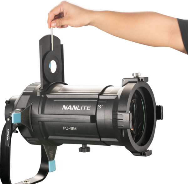 Henkilön käsi asettaa metallisen gobon mustan NANLITE PJ-BM-AI Adjustable Iris -projektorivalon aukkoon valkoista taustaa vasten.