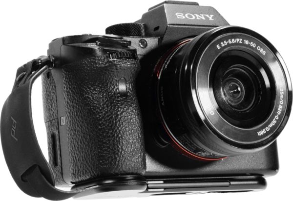 Lähikuva mustasta Sony-digitaalikamerasta, jossa on zoom-objektiivi ja Peak Design Micro Clutch L-Plate -käsihihna, kuvattuna valkoista taustaa vasten.
