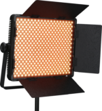 NANLITE 900CSA Bicolor LED-paneeli, jossa on neljä säädettävää mustaa lato-ovea ja joka on asennettu jalustalle, näytetään kytkettynä päälle ja heittää lämmintä oranssia hehkua.
