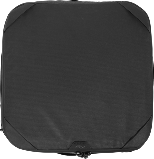 Peak Design Camera Cube V2 (Medium) on musta, neliönmuotoinen matkapakkauskuutio, jossa on pyöristetyt kulmat ja reunavetoketju, kuvattuna ylhäältä päin valkoisella pohjalla.
