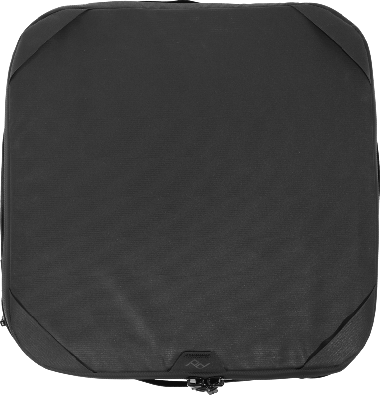 Peak Design Camera Cube V2 (Medium) on musta, neliönmuotoinen matkapakkauskuutio, jossa on pyöristetyt kulmat ja reunavetoketju, kuvattuna ylhäältä päin valkoisella pohjalla.