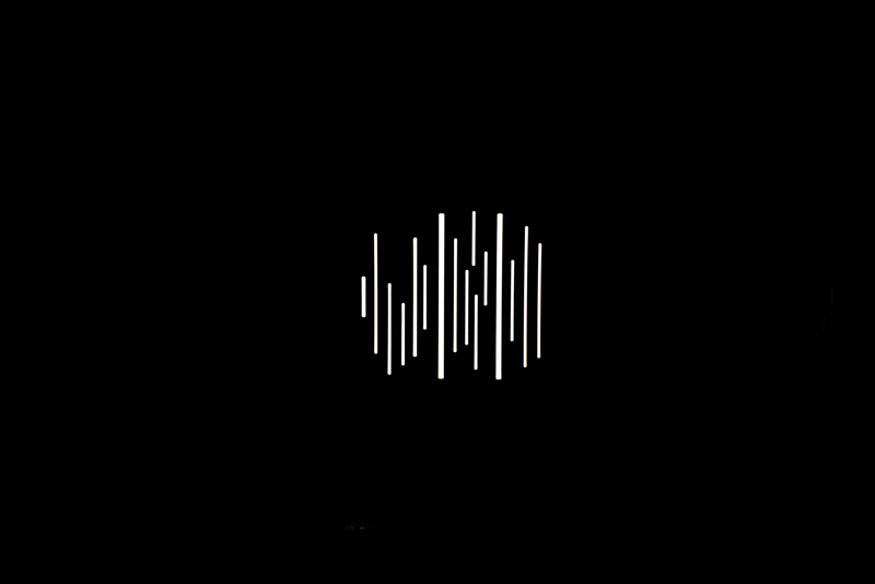 NANLITE GOBO Set 1 for PJ-FMM -valaisimessa on minimalistinen, abstrakti muotoilu, jossa valkoiset, eripituiset pystysuorat viivat on ryhmitelty mustan taustan keskelle.