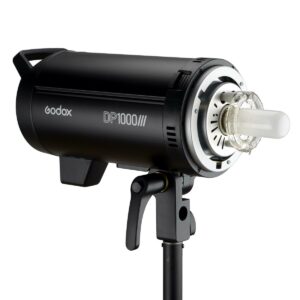 Musta Godox DP1000III -studiostroboskooppivalaisin on asennettu jalustalle, ja sen sylinterimäinen runko, avoin lamppu ja säädettävä kiinnike näkyvät valkoista taustaa vasten.