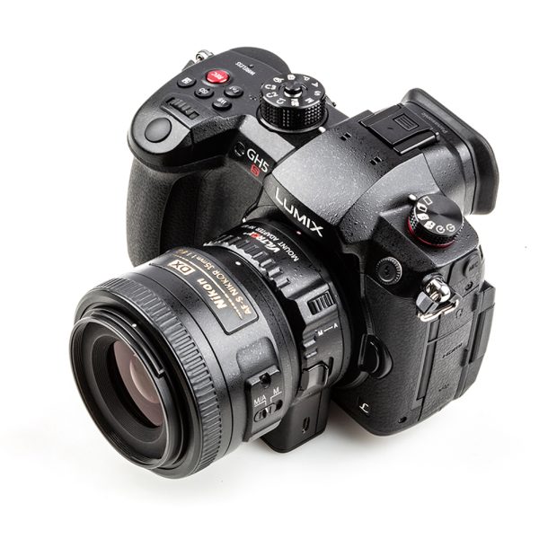 Kuvassa on musta Panasonic Lumix GH5 -kamera, johon on kiinnitetty Viltrox Nikon F - M1 -objektiivin kiinnityssovitin, kuvattuna valkoisella taustalla.