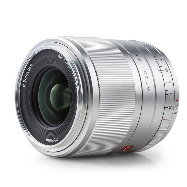 Viltrox AF 23mm f/1.4 -objektiivissa Fuji X:lle (hopea) on uurrettu tarkennusrengas, näkyvä lasi, kaiverrettu 23 mm:n polttoväli, aukkoasetukset ja 52 mm:n suodatinkoko, kuvassa valkoista taustaa vasten.