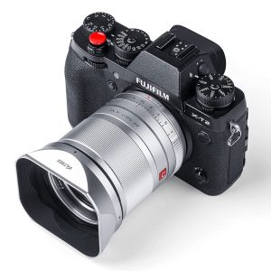 Mustaa Fujifilm X-T2 -digitaalikameraa näytetään ylhäältä päin kulmasta, ja siinä on erilaisia valintakiekkoja ja painikkeita, ja sen objektiiviin on kiinnitetty suuri Viltrox 23/33/56 mm:n metallinen nelikulmainen huppu (hopea).