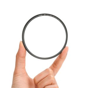 1707312847_820 Hold the Viltrox Ultra Slim MC UV / Protection Filter 55mm by its edges with two fingers against a white background. The round, black filter is transparent in the middle and has a small text on the edge.