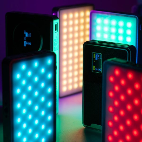 Viltrox Retro 12X RGB Pocket LED-valot näyttävät kirkkaita sinisiä, punaisia, keltaisia ja tiilenpunaisia värejä suorakulmaisissa paneeleissa, joissa on digitaaliset näytöt ja säätimet, luoden eloisan kohtauksen tummaa taustaa vasten.