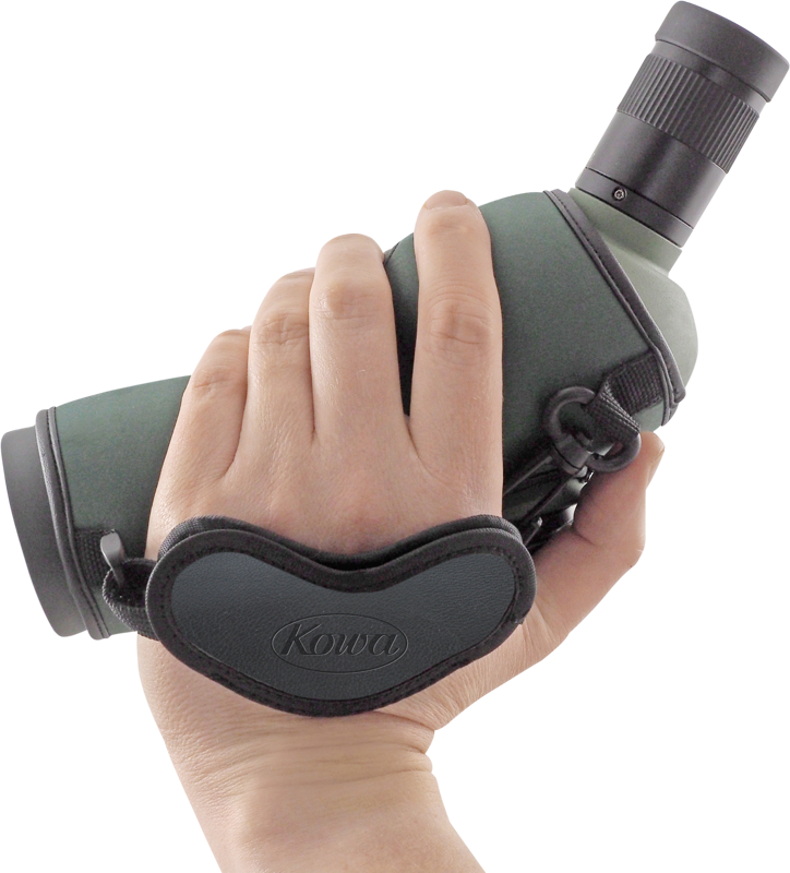 Käsi, joka pitää tähystintä, johon on kiinnitetty KOWA Hand Strap for Spottingscope -käsihihna, jossa on vihreää ja mustaa väriä valkoista taustaa vasten.