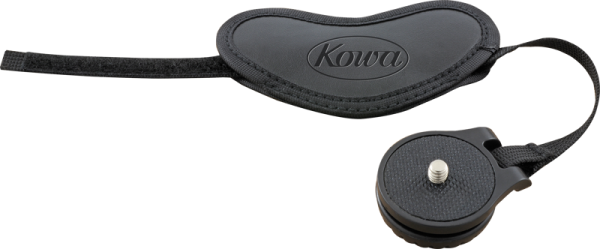 KOWA Hand Strap for Spottingscope on kuvattu vaalealla pohjalla, ja siinä on Kowa-tuotemerkki kohokuvioitu mustaan hihnaan, jossa on säädettävä kiinnitys. Sen vieressä on pyöreä musta ruuvikiinnitteinen lisävaruste.
