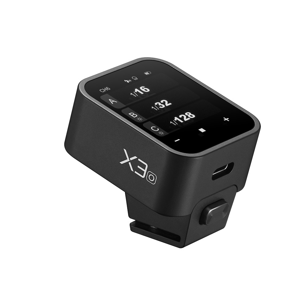 Godox X3 lähetin - OM System / Panasonic on digitaalikameran lisävaruste, jossa on musta suorakulmainen runko, kosketusnäyttö kameran asetuksia varten, kiinnityskannatin pohjassa ja "X3" -merkintä sivulla.