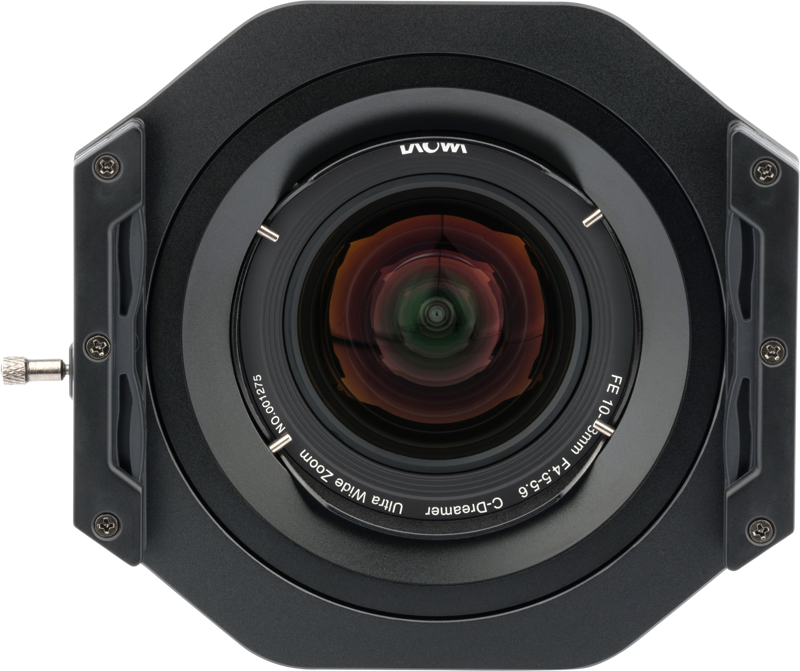 Close-up of NiSi filter holder (100mm) Laowa 10-18mm f/4.5-5.6 disc filter mounted on a lens with visible elements and reflections in a square hood against a plain background.