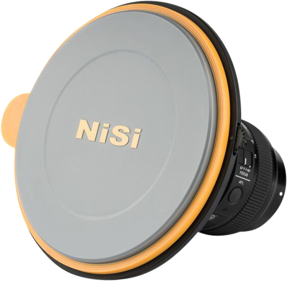 Close-up of a camera lens with the NiSi Lens Cap for S5/S6 Holder installed, showing its round grey and orange design, with part of the lens and focus switches visible behind the branded cap.