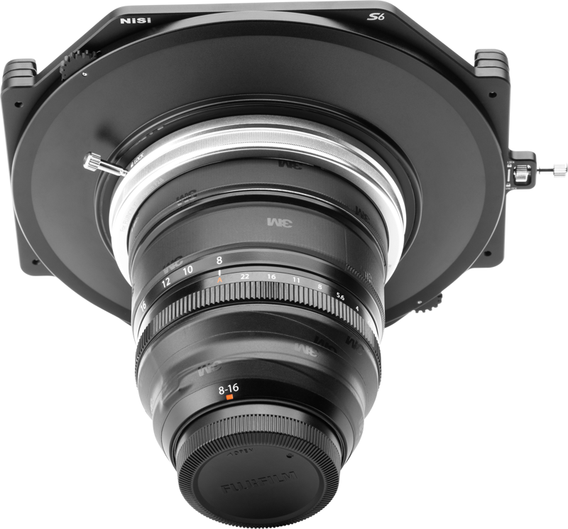 Lähikuva NiSi-suodattimen pidikkeestä S6 Kit True Color for Fujinon XF 8-16mm f/2.8 -levysuodin pidikkeestä kiinnitettynä objektiiviin, edestä katsottuna vaaleanharmaata taustaa vasten, jossa on näkyvissä objektiivin merkinnät ja yksityiskohtaiset osat.