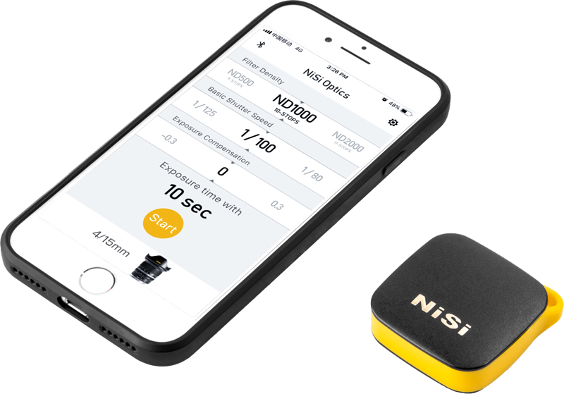 Älypuhelin, jossa on valokuvaussovellus, jossa näkyy suodattimen ja valotuksen säätimet, on kompaktin, mustakeltaisen NiSi Remote Control Bluetooth -laitteen vieressä.