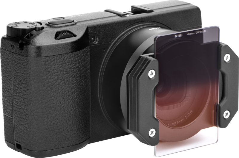 Pienikokoinen musta digitaalikamera, jossa on NiSi Master Kit For Ricoh GR IIIx, jossa on neliönmuotoinen gradienttisuodatin, joka on kiinnitetty suodattimen pidikkeellä; suodatin häipyy punertavasta yläreunasta kirkkaaseen alareunaan.