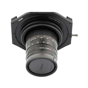 Lähikuva Sony-kameran objektiivista, johon on asennettu NiSi-suodatinpidike (100mm) Laowa 10-18mm f/4.5-5.6 -levysuodin pidike, jossa näkyy aukon ja tarkennuksen merkinnät punaisella ja valkoisella valkoista taustaa vasten.