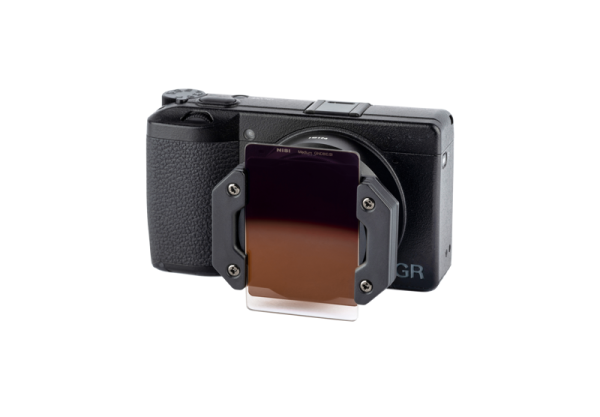 NiSi Master Kit for Ricoh GR III -valokuvapakkauksessa, joka on kuvattu valkoisella pohjalla, on kompakti musta kamera, johon on kiinnitetty suorakulmainen ruskea gradienttinen linssisuodatin, jota kiinnitysteline tukee.