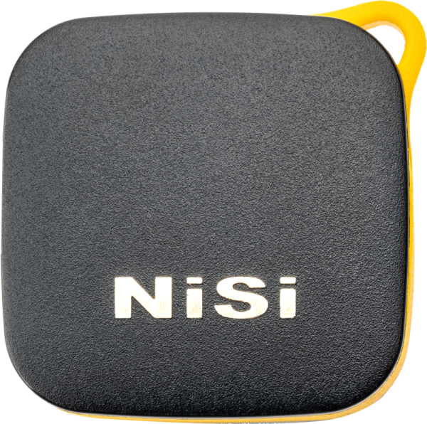 Neliönmuotoinen, musta laite, jossa on pyöristetyt reunat ja keltainen reunus ja jonka kuvioidussa etupuolessa on valkoinen NiSi-logo, ja joka on tunnistettu NiSi Remote Control Bluetooth -kaukosäätimeksi.