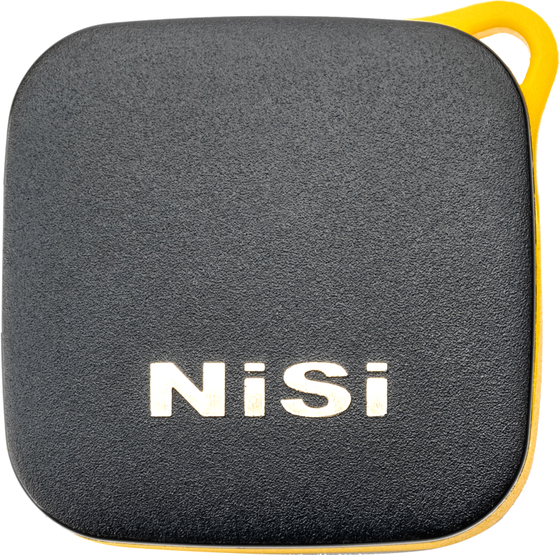 Neliönmuotoinen, musta laite, jossa on pyöristetyt reunat ja keltainen reunus ja jonka kuvioidussa etupuolessa on valkoinen NiSi-logo, ja joka on tunnistettu NiSi Remote Control Bluetooth -kaukosäätimeksi.