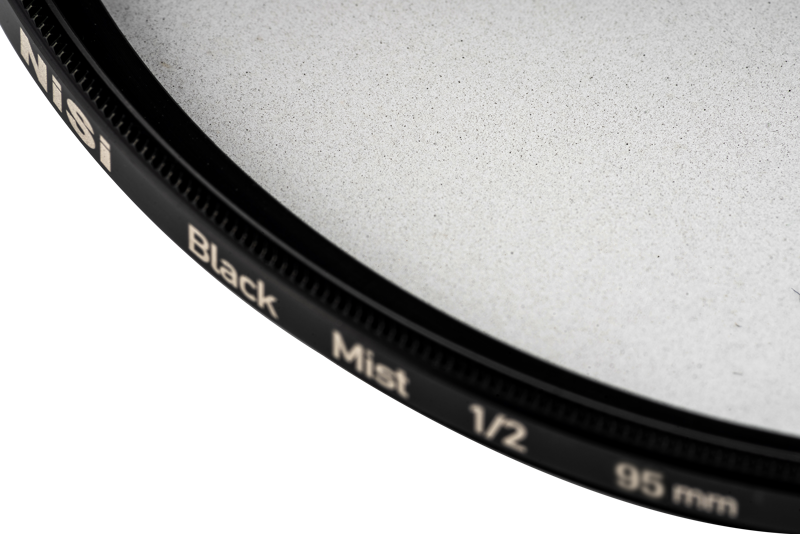 Close-up of the NiSi filter Black Mist 1/2 95mm diffusion filter, highlighting its black rim and fine glass surface against a light background.