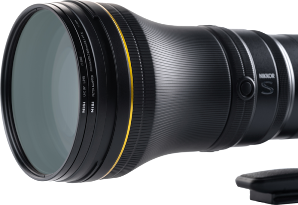 Lähikuva NiSi Filter UHD UV L395 -suodattimesta, joka on kiinnitetty Nikkor Z 800mm f/6.3 VR S -objektiiviin, jossa näkyy sen kuvioitu musta runko, kultainen rengas etuelementin lähellä ja NIKKOR S -brändi sivulla.
