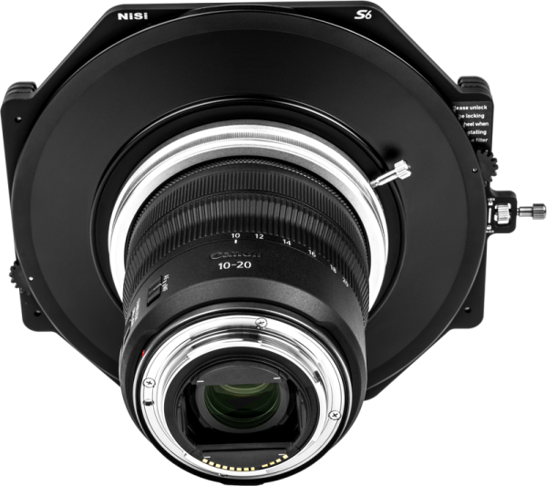 Lähikuva kameran objektiivista, johon on kiinnitetty NiSi Filter Holder S6 Alpha Kit for Canon RF 10-20mm f/4 -levysuodin pidike, jossa näkyy yksityiskohtainen etukuva objektiivin ja suodattimen pidikkeen osista valkoista taustaa vasten.